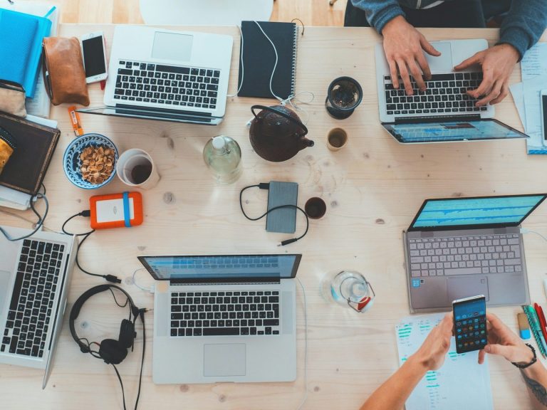 Vistas aéreas de una mesa con laptops, teléfonos y snacks en un entorno de trabajo colaborativo.